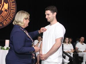graduate in white scrubs getting pin on chest
